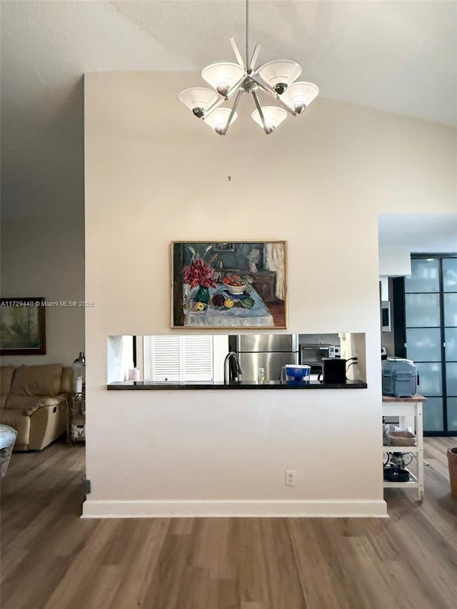 kitchen featuring a notable chandelier, wood-type flooring, lofted ceiling, and stainless steel fridge