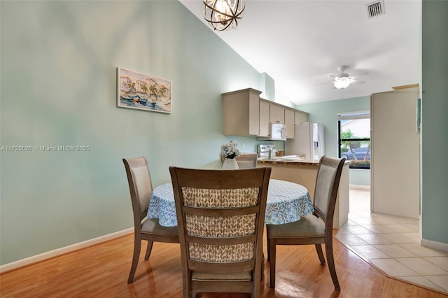 dining room with vaulted ceiling, ceiling fan with notable chandelier, and light hardwood / wood-style floors