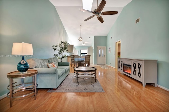 living room with high vaulted ceiling, light hardwood / wood-style flooring, ceiling fan, and a fireplace