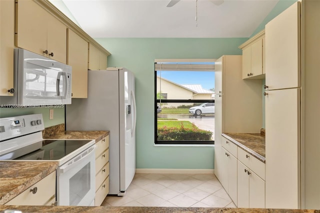 kitchen with white appliances, light tile patterned floors, lofted ceiling, and cream cabinetry