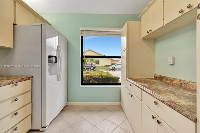 kitchen featuring white fridge with ice dispenser, dark stone counters, cream cabinetry, and light tile patterned flooring