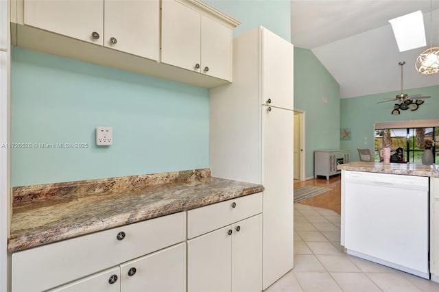 kitchen with white dishwasher, light tile patterned floors, lofted ceiling with skylight, and dark stone countertops