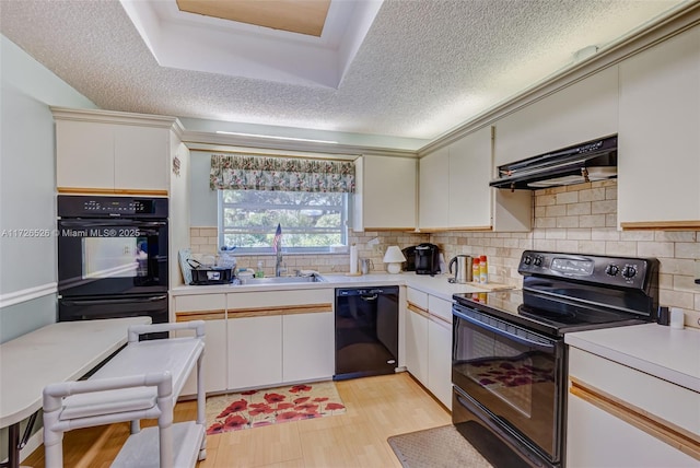 kitchen with black appliances, range hood, white cabinets, and sink