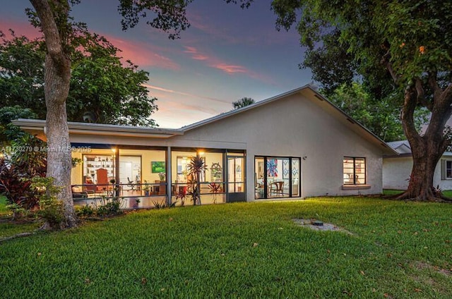 back house at dusk featuring a lawn