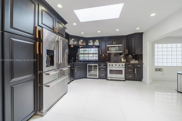 kitchen featuring a skylight, tasteful backsplash, sink, beverage cooler, and high end appliances