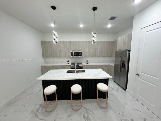 kitchen featuring decorative light fixtures, a center island with sink, light stone counters, and appliances with stainless steel finishes