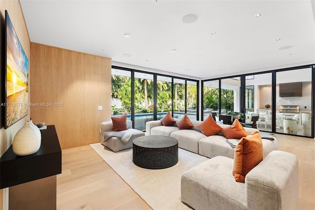 living room with a wall of windows, light hardwood / wood-style flooring, and wooden walls