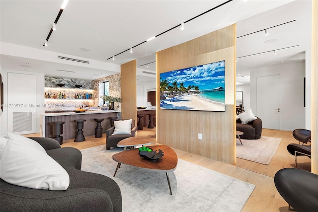 living room with indoor bar, rail lighting, light wood-type flooring, and wooden walls