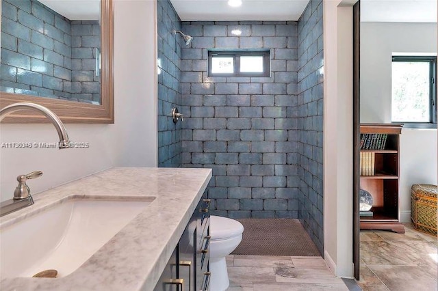 bathroom featuring a tile shower, vanity, a wealth of natural light, and toilet