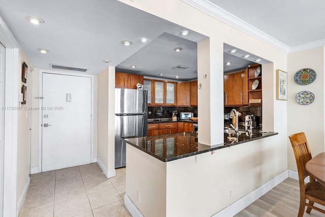 kitchen with crown molding, tasteful backsplash, dark stone countertops, stainless steel fridge, and kitchen peninsula