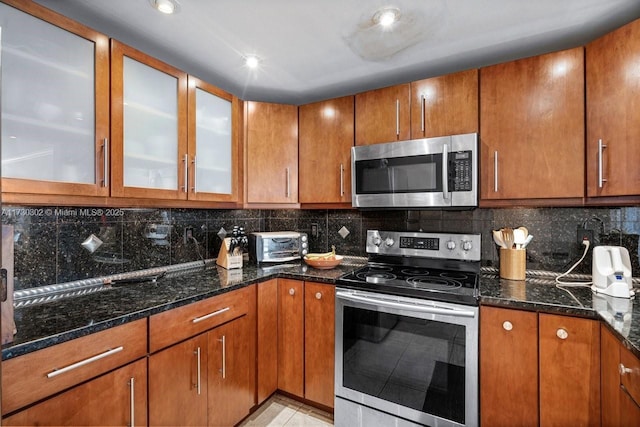 kitchen featuring tasteful backsplash, stainless steel appliances, dark stone counters, and light tile patterned flooring