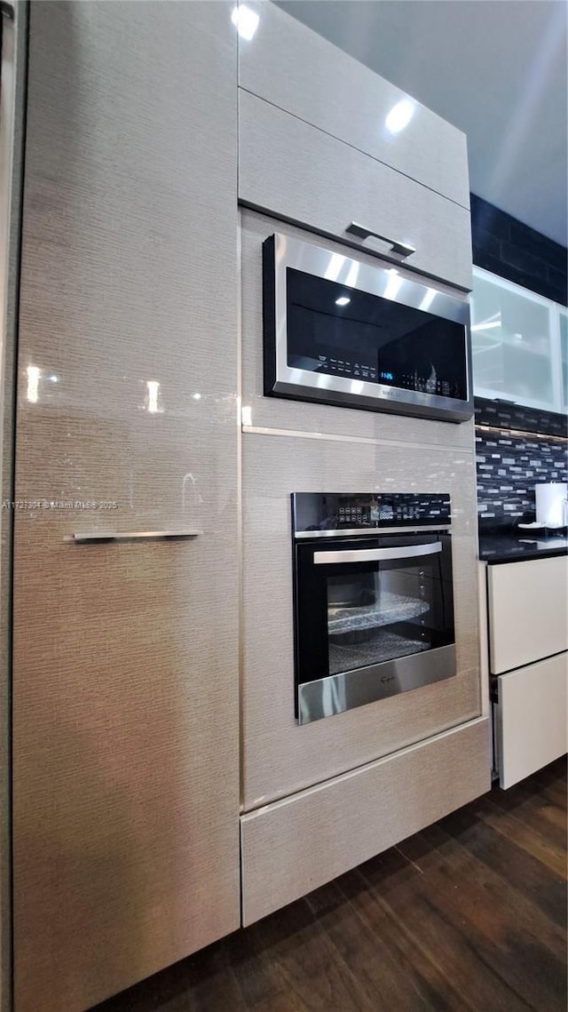 kitchen with dark wood-type flooring, white cabinets, appliances with stainless steel finishes, and tasteful backsplash