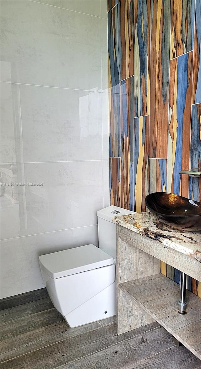 bathroom with hardwood / wood-style flooring, toilet, and tile walls