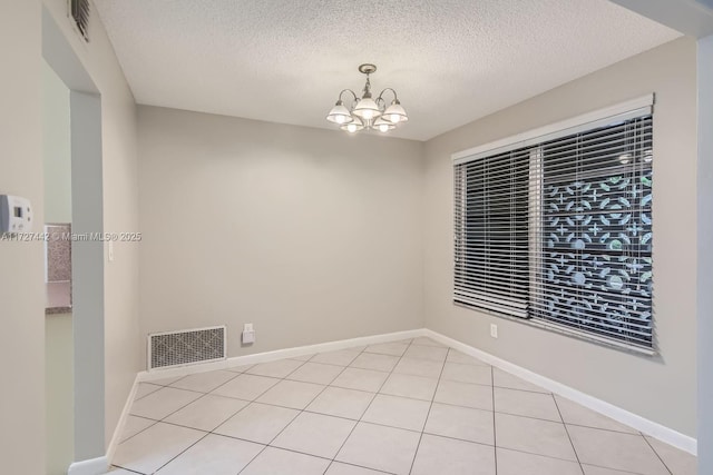 empty room featuring an inviting chandelier, light tile patterned floors, and a textured ceiling