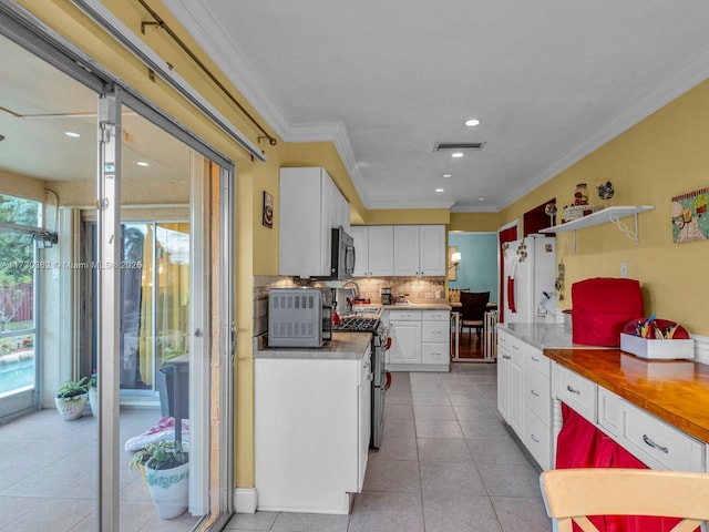 kitchen featuring white cabinets, appliances with stainless steel finishes, decorative backsplash, light tile patterned floors, and crown molding