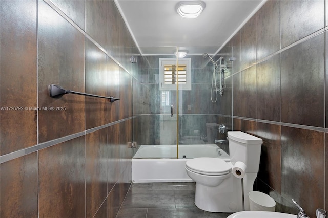 bathroom featuring bath / shower combo with glass door, toilet, and tile walls