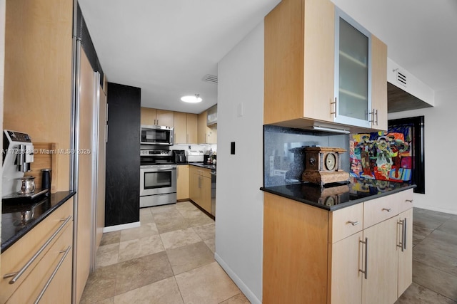 kitchen with dark stone countertops, decorative backsplash, light brown cabinetry, and appliances with stainless steel finishes