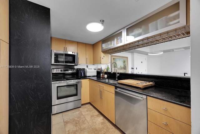 kitchen featuring appliances with stainless steel finishes, light brown cabinets, dark stone counters, sink, and light tile patterned floors