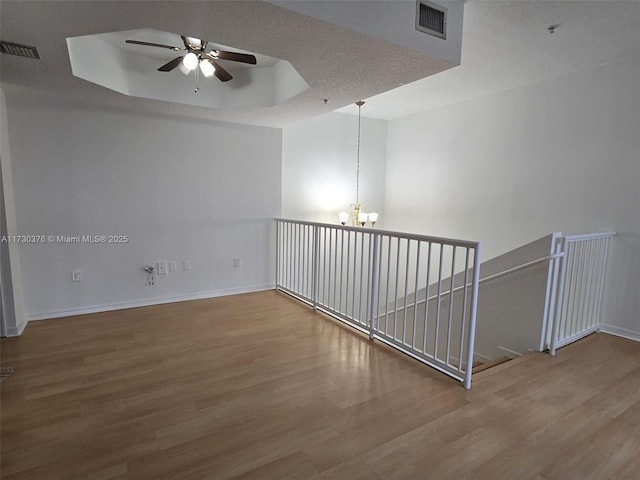 empty room featuring ceiling fan with notable chandelier, a raised ceiling, and hardwood / wood-style floors