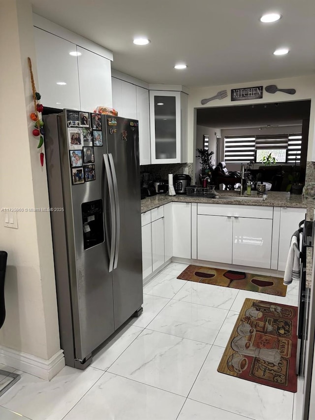 kitchen featuring decorative backsplash, white cabinets, dark stone countertops, sink, and stainless steel fridge