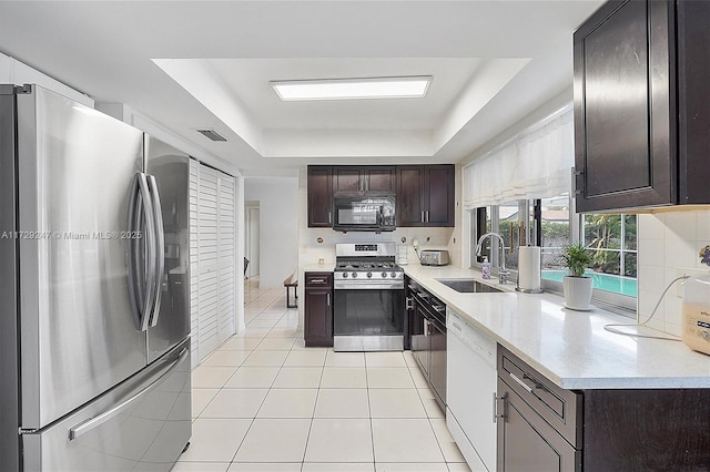 kitchen with dark brown cabinetry, appliances with stainless steel finishes, sink, a raised ceiling, and light tile patterned flooring