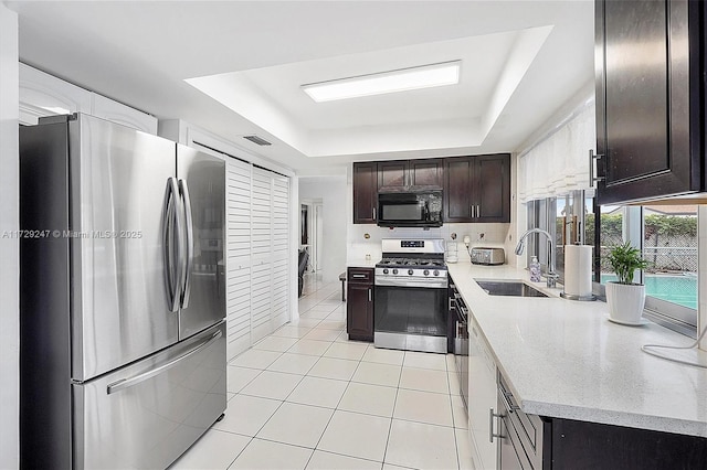 kitchen with dark brown cabinetry, appliances with stainless steel finishes, sink, light tile patterned floors, and a tray ceiling