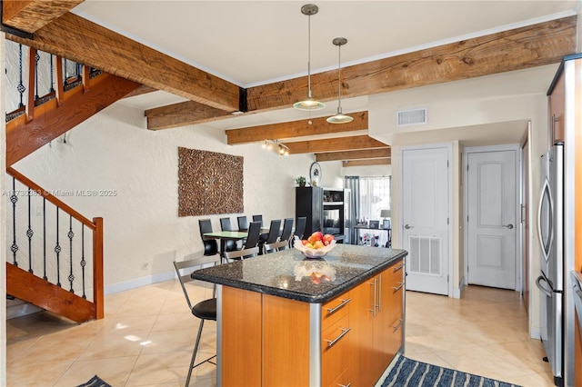 kitchen featuring a breakfast bar, a center island, dark stone countertops, stainless steel refrigerator, and beam ceiling