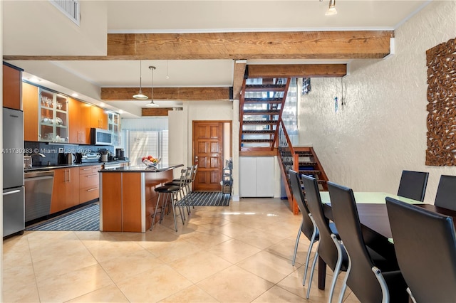 kitchen featuring a breakfast bar area, decorative light fixtures, light tile patterned floors, beamed ceiling, and stainless steel appliances