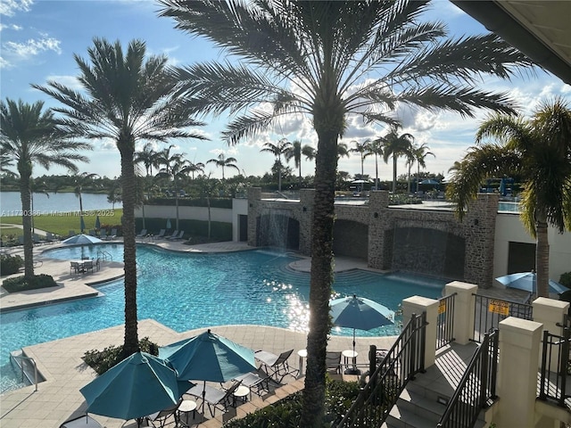 view of pool featuring pool water feature, a water view, and a patio