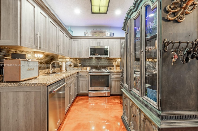 kitchen with a textured ceiling, stainless steel appliances, decorative backsplash, sink, and light stone counters