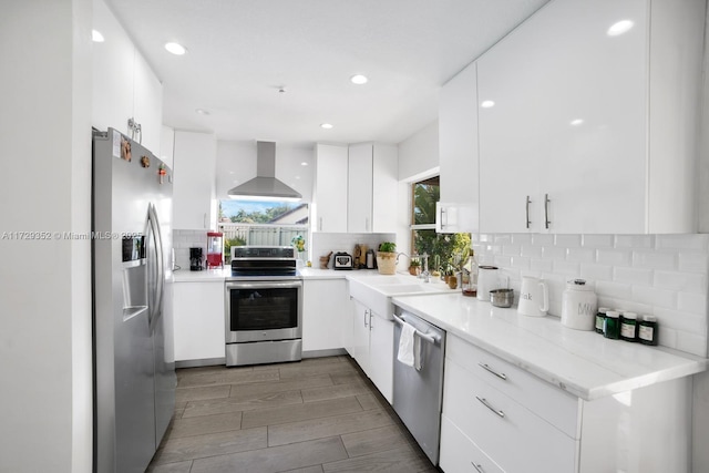 kitchen with appliances with stainless steel finishes, sink, white cabinets, tasteful backsplash, and wall chimney range hood