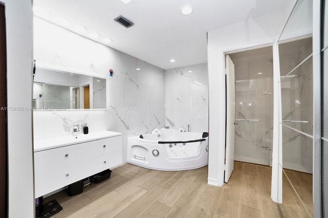 bathroom with a tub, tile walls, wood-type flooring, and vanity