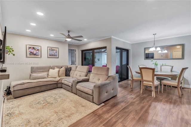 living room with ceiling fan with notable chandelier, ornamental molding, and dark wood-type flooring