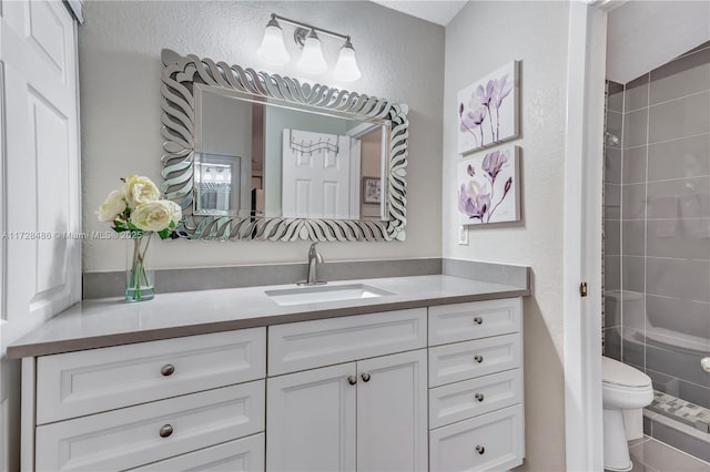 bathroom with toilet, vanity, and tiled shower