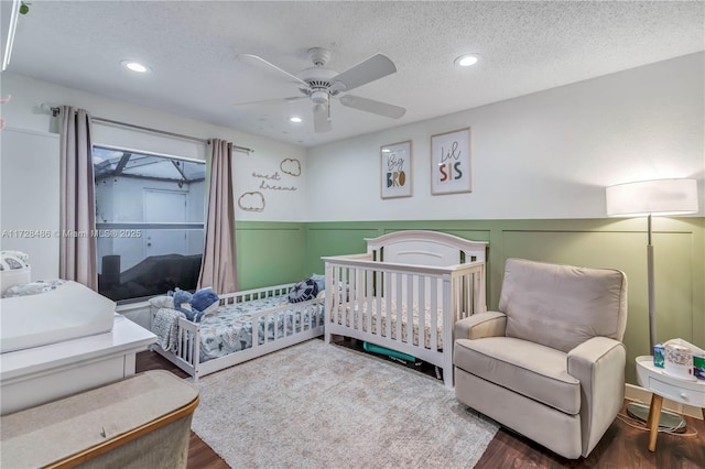 bedroom with ceiling fan, wood-type flooring, a nursery area, and a textured ceiling