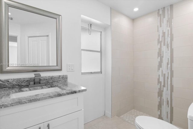 bathroom featuring toilet, vanity, and a tile shower