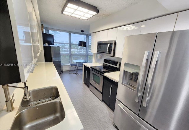 kitchen with a textured ceiling, white cabinets, a wall of windows, stainless steel appliances, and sink