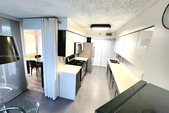 kitchen with sink, white cabinets, a textured ceiling, and stainless steel appliances