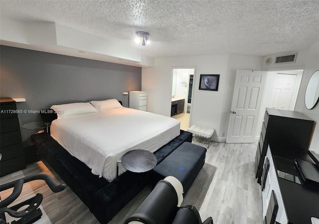 bedroom with light wood-type flooring, a textured ceiling, and connected bathroom