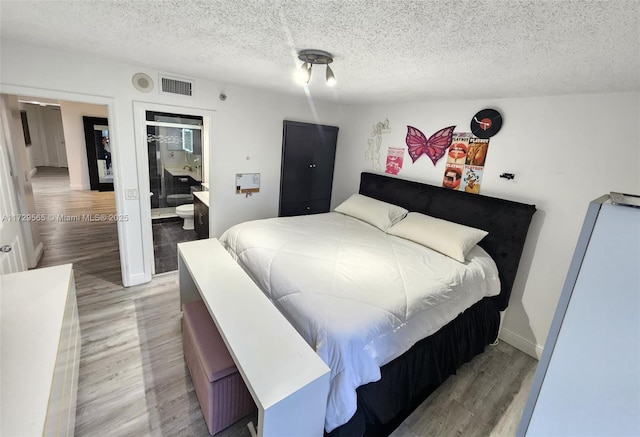 bedroom with hardwood / wood-style flooring, a textured ceiling, and connected bathroom