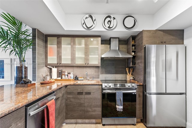 kitchen featuring appliances with stainless steel finishes, wall chimney exhaust hood, sink, backsplash, and light stone counters