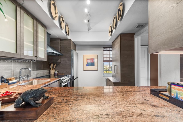 kitchen with track lighting, wall chimney range hood, sink, stainless steel appliances, and light stone counters