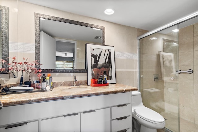 bathroom featuring a shower with door, toilet, vanity, and tile walls