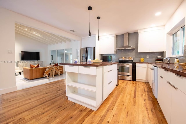 kitchen featuring white cabinets, decorative light fixtures, wall chimney range hood, stainless steel appliances, and tasteful backsplash