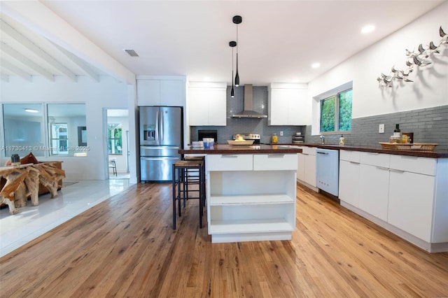 kitchen featuring decorative light fixtures, white cabinetry, wall chimney range hood, stainless steel appliances, and beamed ceiling