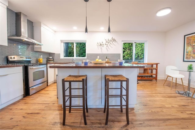 kitchen with decorative light fixtures, white cabinets, stainless steel range with electric cooktop, wall chimney range hood, and a breakfast bar area