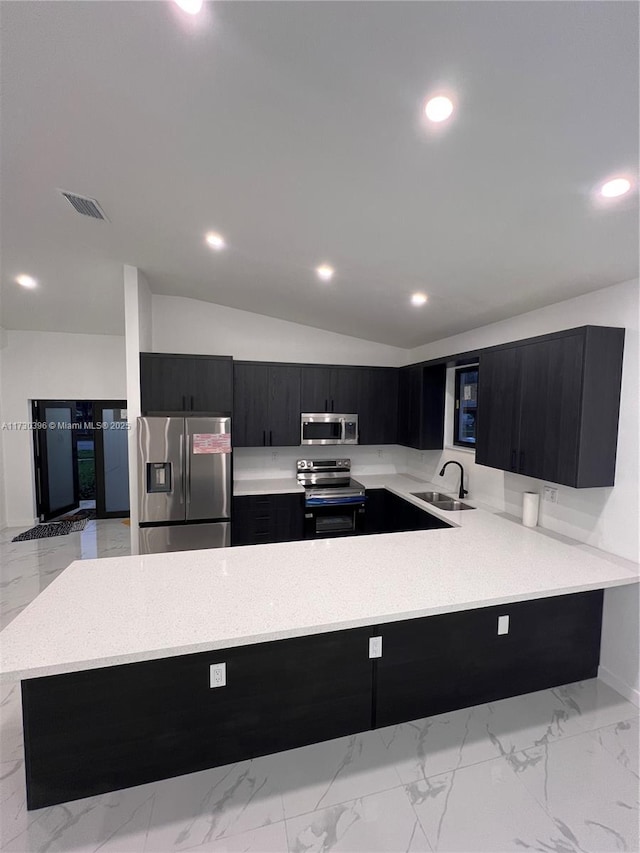 kitchen featuring lofted ceiling, a peninsula, a sink, appliances with stainless steel finishes, and dark cabinetry