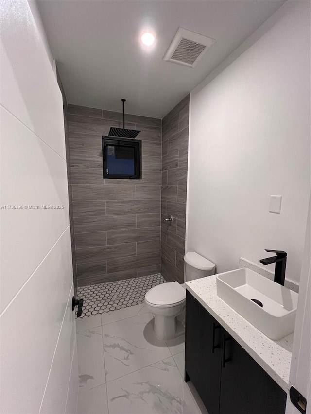 bathroom featuring a tile shower, toilet, and vanity