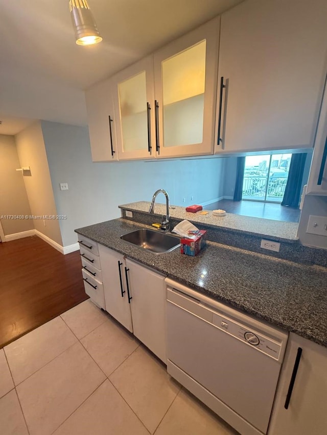 kitchen with white dishwasher, white cabinetry, light tile patterned floors, sink, and dark stone counters