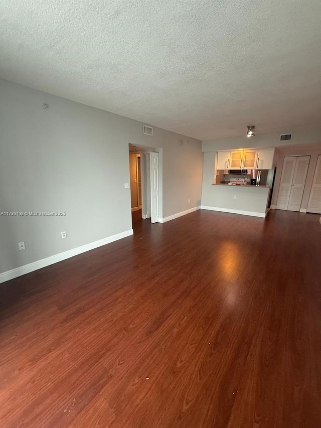 unfurnished living room with a textured ceiling and dark hardwood / wood-style flooring